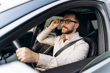 Gülümseyen, kendinden emin orta yaşlı bir işadamı şık gözlükler takıyor, yeni bir araba sürüyor, direksiyon tutuyor, başka tarafa bakıyor. Ulaşım, sigorta kavramı