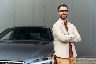 Gülümseyen, şık gözlükler takan yakışıklı bir adamın portresi ve yeni arabanın yanında durup kameraya bakan çapraz kollu sıradan kıyafetler. Ulaşım kavramı