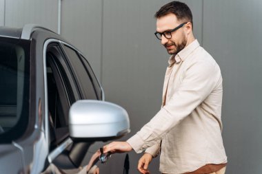 Mutlu, gülümseyen, gözlüklü, araba kapısı açık, yeni arabanın yanında duran sakallı bir adamın portresi. Ulaşım kavramı