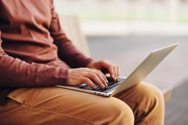 İşadamı dizüstü bilgisayarla çalışıyor, kanepenin üstünde oturuyor, ellere odaklanıyor. Kopya yazarı klavyeye yazı yazıyor. Çevrimiçi teknoloji kavramı