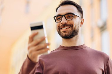 Gülümseyen, gözlük takan, cep telefonu takan cep telefonu kullanan, cep telefonu uygulaması kullanan, kısa mesaj çeken, video izleyen sakallı bir adamın portresi. Sosyal medya kavramı