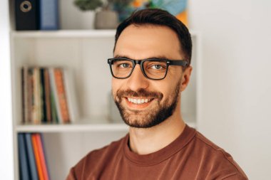 Mutlu, gülümseyen, gözlüklü, kameraya bakan, modern ofiste duran sakallı bir adamın portresi. Diş sağlığı konsepti