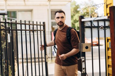 Sırt çantası tutan yakışıklı Latin bir adamın portresi, öğrencinin kapı anahtarı, açık kapı.