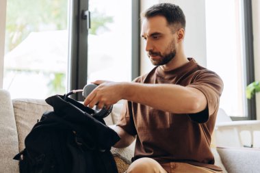 Sakallı iş adamının portresi sırt çantasında, dizüstü bilgisayarı tutarak, kafede oturarak eşyaları bir araya getirdi. İş konsepti