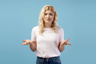 Üzgün, kafası karışmış bir gencin portresi, günlük kıyafetler giyen, kameraya bakan, mavi arka planda yalnız poz veren bir kız. Reklam kavramı