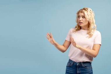 Korkmuş, şok olmuş genç kız portresi, gözlerini kaçıran genç kız, mavi arka planda tek başına duruyor, kopyalama alanı. Reklam kavramı