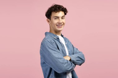 Gülümseyen, yakışıklı, mutlu genç çocuk, günlük kıyafetler giymiş, pembe arka planda izole bir şekilde duran çapraz kollu kameraya bakıyor. Reklam, alışveriş konsepti