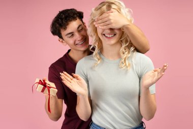 Mutlu, gülümseyen bir çiftin portresi kız arkadaşının gözlerini hediye kutusuyla kaplayan pembe arka planda tek başına duran bir erkek arkadaş. Sevgililer Günü konsepti