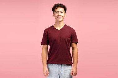 Gülümseyen, diş teli takan, kırmızı tişörtlü, kameraya bakan, pembe arka planda yalnız poz veren çekici bir gencin portresi. Diş sağlığı konsepti