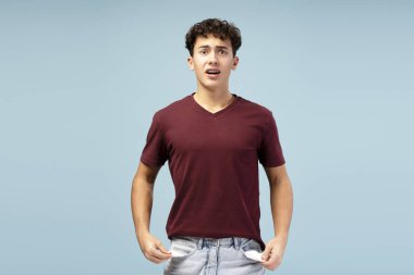 Sıradan kıyafetler giyen, boş cepleri gösteren, kameraya bakan, mavi arka planda tek başına duran mutsuz bir gencin portresi. Reklam kavramı