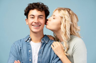 Mutlu, gülümseyen gençlerin portresi, çift, diş telleriyle kameraya bakan güzel kız çocuğu, mavi arka planda tek başına duruyor. Aşk, flört, ilişki konsepti