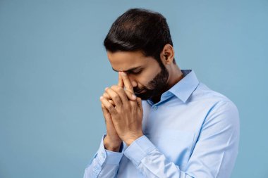 Sakallı, orta yaşlı Hintli bir adamın portresi. Mavi arka planda tek başına durmuş, gözleri kapalı dua eden bir adam. Din kavramı