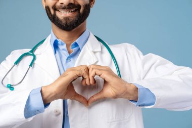 Gülümseyen, sakallı Hintli bir adamın portresi, profesyonel doktor elleriyle ocağı gösteriyor, seçici bir odak noktası, mavi arka planda izole edilmiş yakın plan. Sağlık hizmeti kavramı