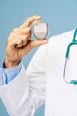 Portrait of professional doctor, cardiologist holding pacemaker selective focus on hands, closeup standing isolated on blue background. Treatment, cardiology concept clipart