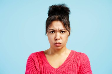 Studio portrait of a young woman frowning and showing displeasure, conveying negative emotions against a vibrant blue backdrop clipart