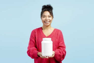 Beyaz plastik bir destek kavanozu tutan gülümseyen bir kadının stüdyo fotoğrafı. Üzerinde boş etiket var. Sağlık ve sağlığı destekliyor.
