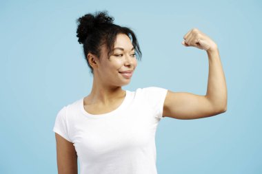 Kaslarını esneten ve mavi arka planda tatmin olmuş bir ifadeyle bakan genç bir kadının stüdyo portresi.