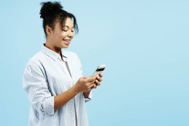 Gülümseyen genç bir kadın akıllı telefonuyla sosyal medyada geziniyor, mobil uygulamalardan hoşlanıyor, online alışveriş yapıyor, sipariş veriyor, arkadaşlarıyla sohbet ediyor.