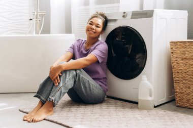 Genç bir kadın banyoda yerde oturuyor, çamaşırlarını yıkadıktan sonra biraz dinleniyor, huzur ve memnuniyet duygusunu kucaklıyor.