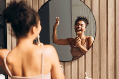 Modern bir banyoda dişlerini fırçalarken şarkı söyleyen mutlu genç kadın sabah rutininin tadını çıkarıyor.