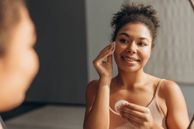 Cilt bakımı için pamuk pedi kullanan genç bir kadın sabah güzellik tedavisinin keyfini çıkarıyor.