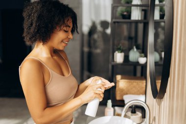 Mutlu kadın nemlendirici losyon kullanıyor, modern banyoda cilt bakımını seviyor, sağlıklı yaşam tarzını ve kişisel bakımını teşvik ediyor.