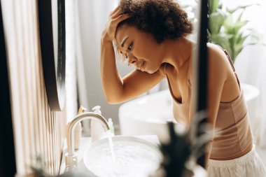 Genç bir kadın banyoda yalnız başına oturuyor, başı dertte, baş ağrısı ve duygusal karışıklığın ağırlığını hissediyor.