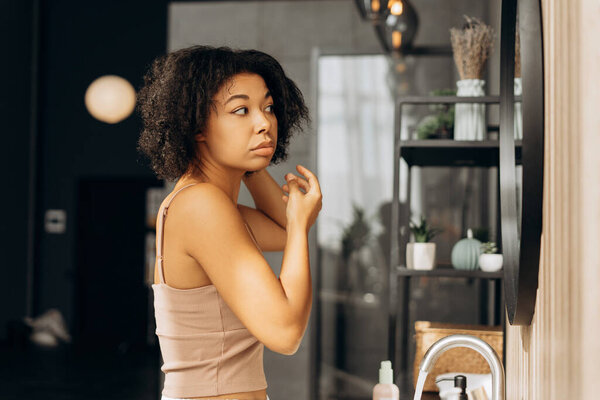 Young woman adjusting her curly hair while looking in the bathroom mirror, getting ready for the day