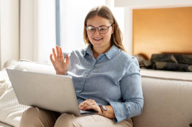 Bilgisayarla çalışırken gülümseyen bir kadının portresi. El sallarken, internette sohbet ederken. Teknoloji, iletişim konsepti