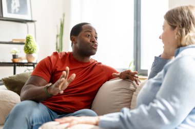 Oturma odasındaki kanepede oturan, birbiriyle konuşan sevimli bir çift. Aile eğlencesi, ilişki konsepti