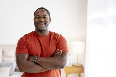 Neşeli orta yaşlı Afrikalı Amerikalı adam kollarını kavuşturup kameraya bakıyor, evde poz veriyor. Yaşam tarzı kavramı