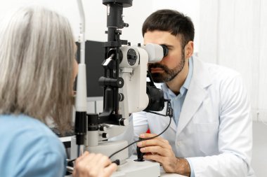 Modern bir göz kliniğinde kesin tanı ve tedavi için yapılan rutin kontroller sırasında yaşlı bir kadın hastanın gözlerini yarık bir lambayla biyomikroskop ile inceliyor.