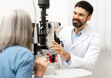 Optometrist is performing an eye examination on a senior patient using a slit lamp, checking her vision and eye health in a medical setting. Vision care concept clipart