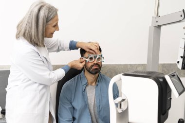 Üst düzey kadın göz doktoru, modern bir klinikte kapsamlı bir göz muayenesi sırasında erkek bir hastanın yüzüne bir fosfor yerleştiriyor.