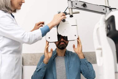 Modern oftalmoloji kliniğinde tıbbi danışmanlık sırasında erkek hastayı muayene ederken, kıdemli kadın göz doktoru foropteri ayarlıyor. Oftalmoloji kavramı