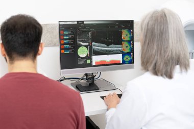 Optik tutarlılık tomografisi taraması yapan kıdemli kadın doktor erkek hastaya bilgisayar ekranında teşhis ve tedavi seçeneklerini modern oftalmoloji kliniğinde açıklıyor.