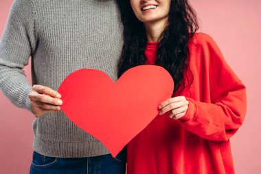 Kocaman kırmızı bir kalp taşıyan gülümseyen çift, sevgililer gününü canlı pembe bir arka plana karşı sevgi, ilgi ve şefkat ile kutluyor, neşe ve beraberliği somutlaştırıyor, seçici bir şekilde ellerine odaklanıyor. Aşk, flört konsepti