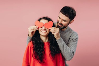 Mutlu çift sevgililer gününü kutluyor, kağıt kalplerle oynuyor, birlikte eğleniyor ve pembe bir arka planda eğleniyorlar.