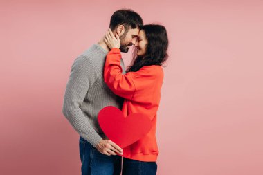 Romantik çift büyük kırmızı bir kalple kucaklaşırken, sevgililer gününü sevgi ve sevgiyle kutlarken, canlı pembe bir arka planda, neşe ve bağlantı yayarak. Sevgililer Günü konsepti