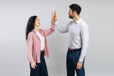 İki mutlu meslektaş birlikte beşlik çakarak başarılarını kutluyorlar. Gri arka planda neşeyle gülümseyen, takım çalışması sergileyen ve iş yerinde güçlü bir ortaklık kuran