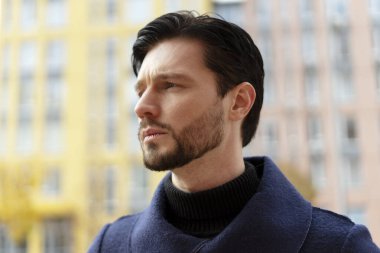 Dışarıya poz veren yakışıklı sakallı genç adamın portresi. Arka plandaki binanın yanında yer alıyor. Yaşam tarzı, şehir hayatı konsepti