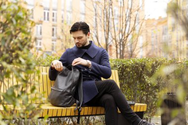 Şehir parkında bankta dizüstü bilgisayarla çalışırken sırt çantası kullanan sakallı bir gencin portresi. Yaşam tarzı, şehir hayatı konsepti