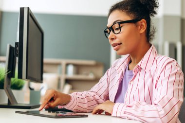 Parlak ofiste modern cihazlarla çalışan, bilgisayar ve tablet üzerinde görevler yapan, çoklu görev ve dijital iş akışını gösteren odaklı çalışan