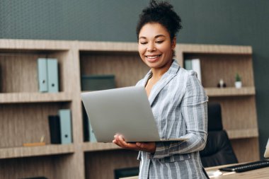 Başarılı bir Afrikalı Amerikalı iş kadını, modern ofiste dizüstü bilgisayar kullanarak klavyede yazı yazan bir metin yazarı. İş konsepti