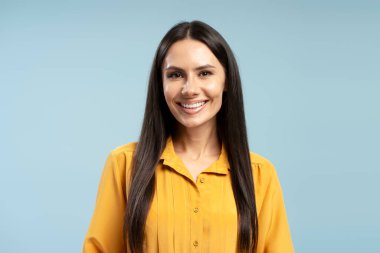 Sarı tişört giyen, mavi arka planda gülümseyen ve poz veren, özgüven ve profesyonellik sergileyen bir iş kadınının stüdyo resmi.