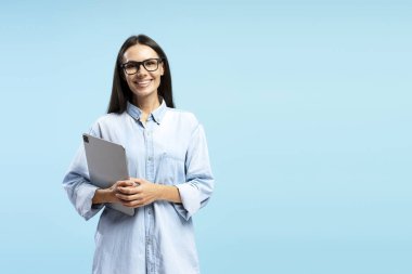 Dijital tablet taşıyan Latin neşeli iş kadınının portresi mavi zemine karşı güven ve profesyonellik yayıyor. Çevrimiçi teknoloji kavramı