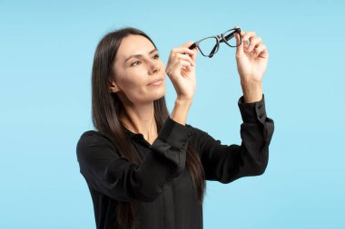 Siyah gömlekli bir iş kadını mavi arka plana bakarken gözlük takıyor. Profesyonel bir ortamda meraka ve derin düşüncelere dalmış. Reklam, alışveriş, vizyon konsepti