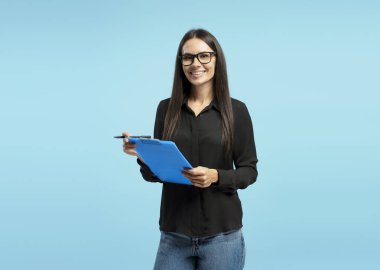 Kendine güvenen iş kadınının portresi gülümseyen ve elinde pano ve kalem tutan, mavi arka planda iş planını sunan, iş dünyasındaki profesyonelliği ve başarıyı gösteren. Reklam kavramı