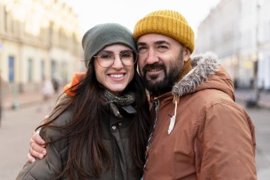 Mutlu çift kışlık giysiler giyiyor, gülümsüyor ve hareketli bir şehir sokağında birbirine sarılıyor serin bir günde, birlikte sıcacık anlarında sıcaklık ve neşe saçıyorlar.