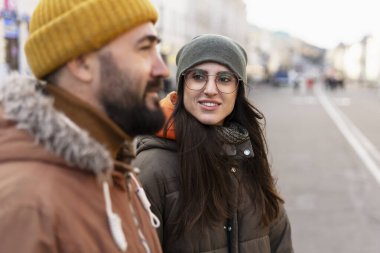 Şık kışlık giysiler ve rahat taksiler giyen mutlu genç çift, serin bir kış gününde sohbet ederken şehrin caddesinde yürür, birlikte vakit geçirirler.
